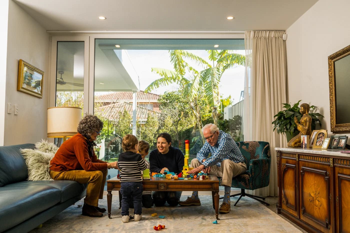A family plays Lego in a TV room with a view of the garden.